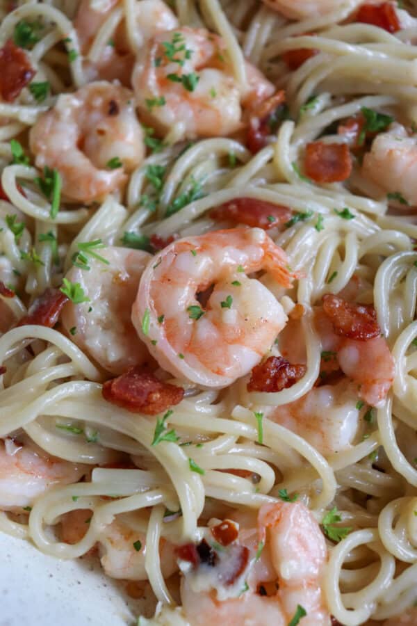 Cooked shrimp in a bed of spaghetti noodles in a white skillet.