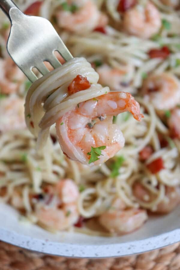 Cooked shrimp on a gold fork with spaghetti and bacon.
