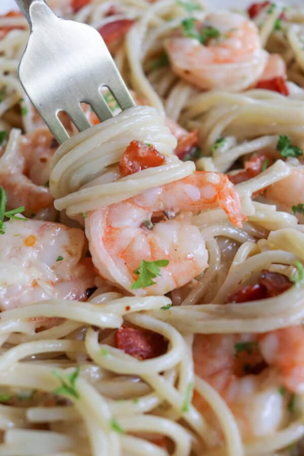 Cooked shrimp on a gold fork with spaghetti and bacon.