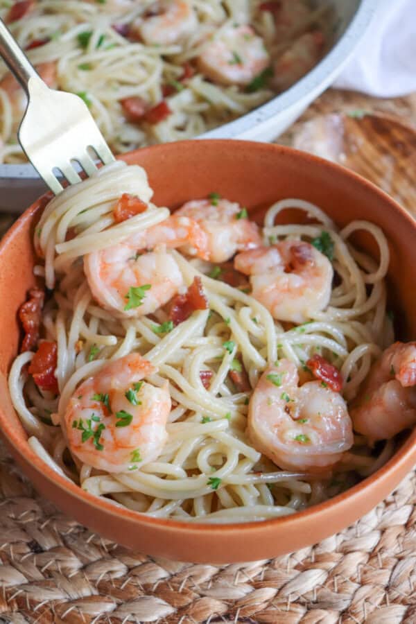 Shrimp spaghetti with bacon in an orange bowl with a fork.