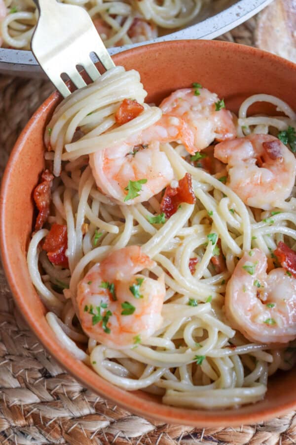 Shrimp spaghetti with bacon in an orange bowl with a fork.