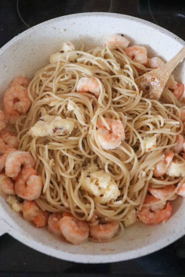 Shrimp, butter and spaghetti mixed in a white skillet.