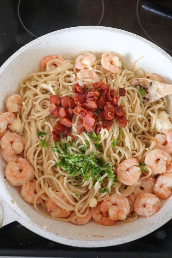 Shrimp and spaghetti in a white skillet topped with bacon bits and fresh parsley.