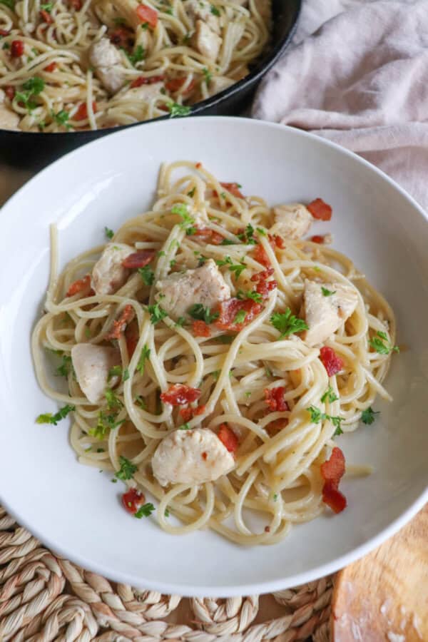 Chicken pasta with bacon bits and spaghetti in a white bowl.