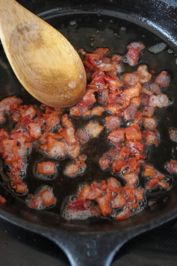 Bacon bits frying in a cast iron skillet.