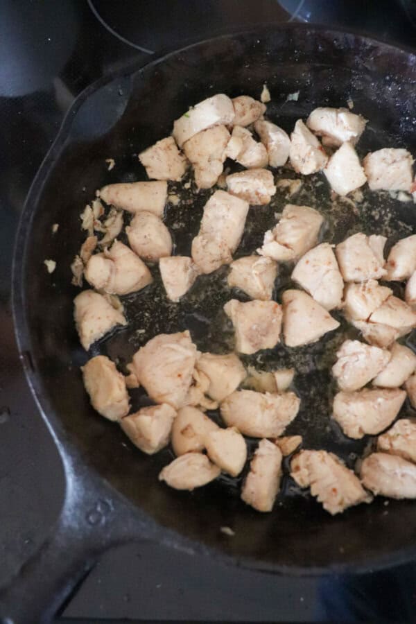 Cubes of chicken fried in a cast iron skillet.