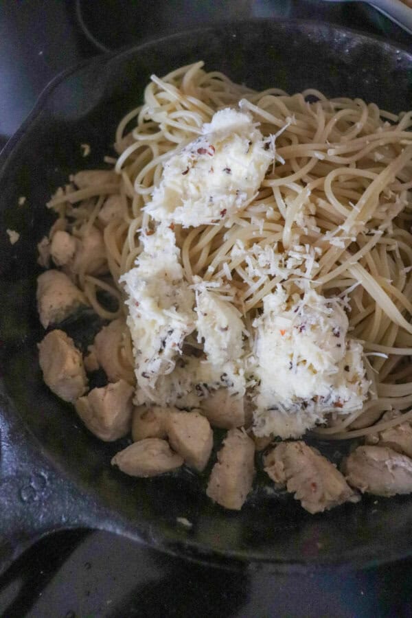 Cooked chicken, spaghetti and herbed butter in a cast iron skillet.
