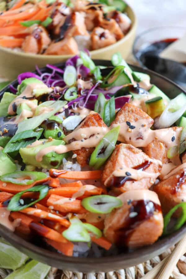 Grilled salmon and vegetables on a bowl of rice drizzled in teriyaki sauce and spicy mayo.