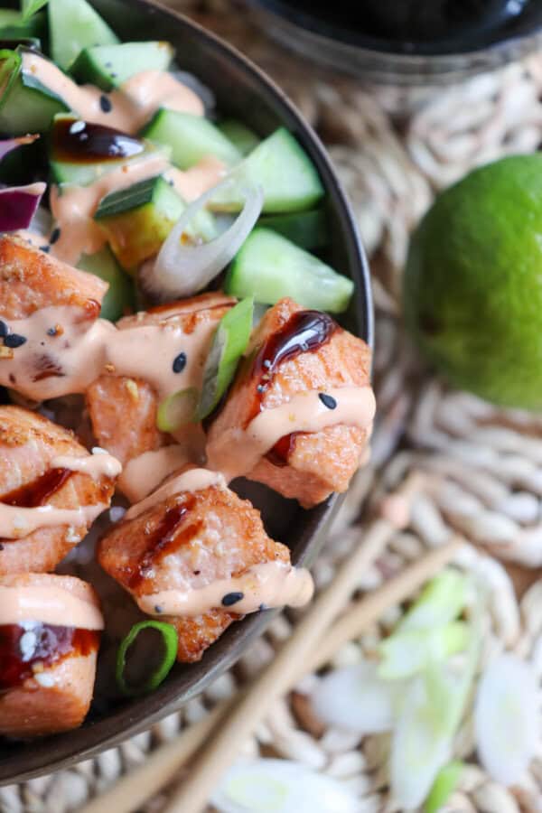 Close up of grilled salmon and vegetables on a bowl of rice drizzled in teriyaki sauce and spicy mayo.
