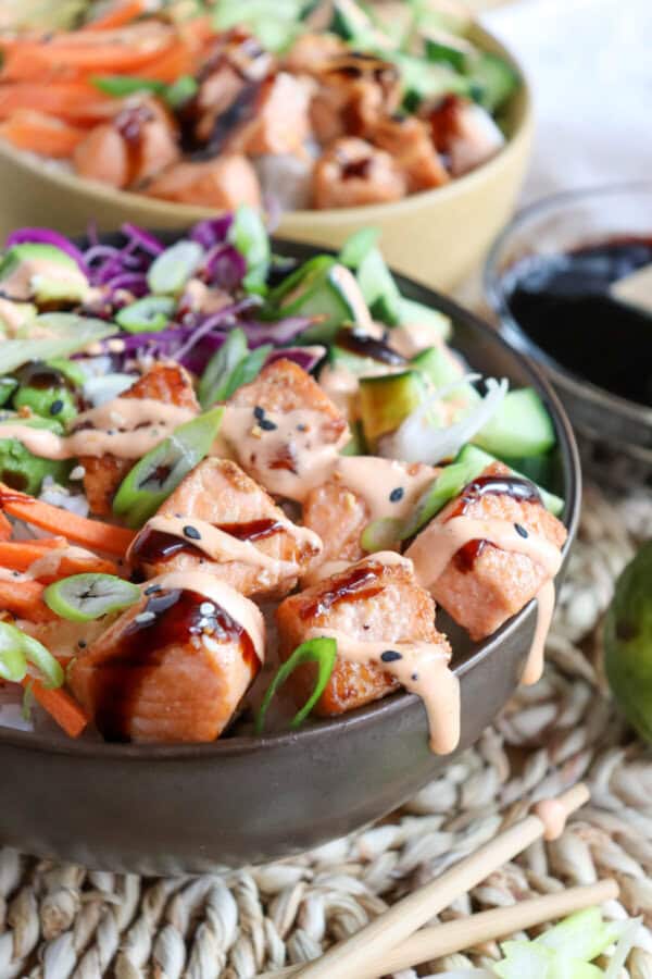 Close up of grilled salmon and vegetables on a bowl of rice drizzled in teriyaki sauce and spicy mayo.