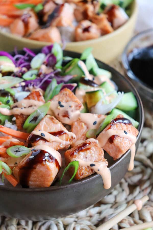 Close up of grilled salmon and vegetables on a bowl of rice drizzled in teriyaki sauce and spicy mayo.
