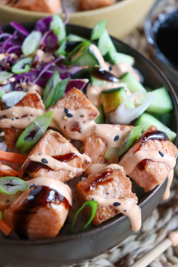 Close up of grilled salmon and vegetables on a bowl of rice drizzled in teriyaki sauce and spicy mayo.