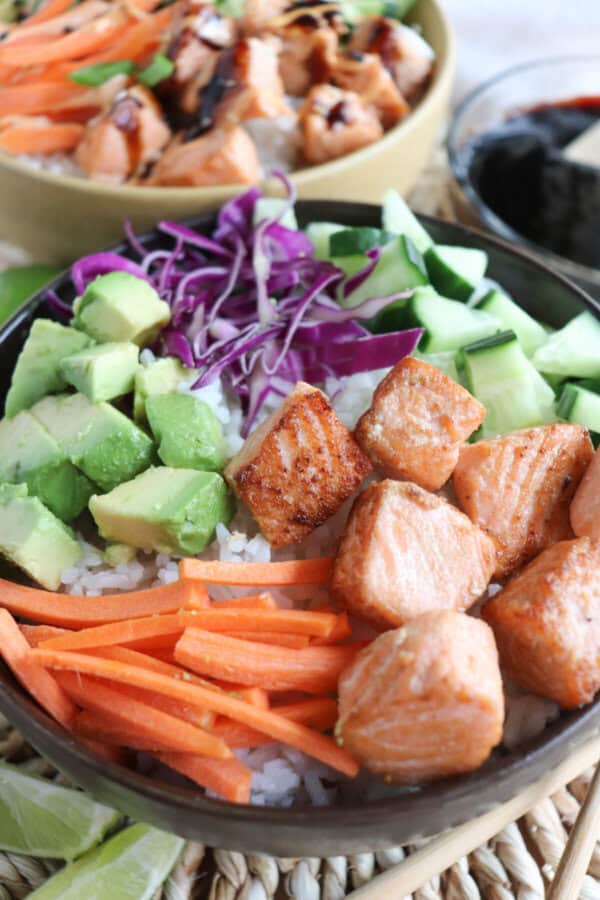 Salmon and vegetables over rice in a black bowl.