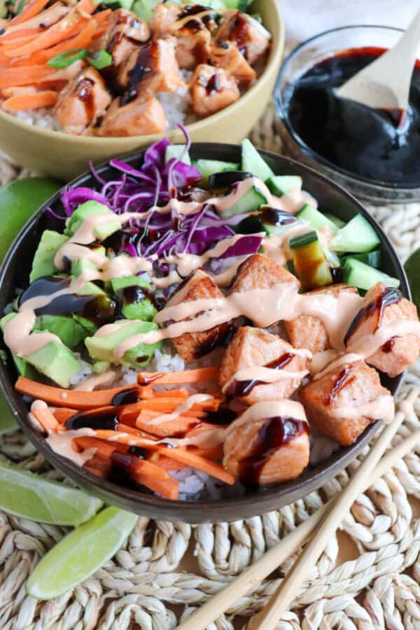 Salmon and vegetables drizzled in spicy mayo and teriyaki sauce in a black bowl.