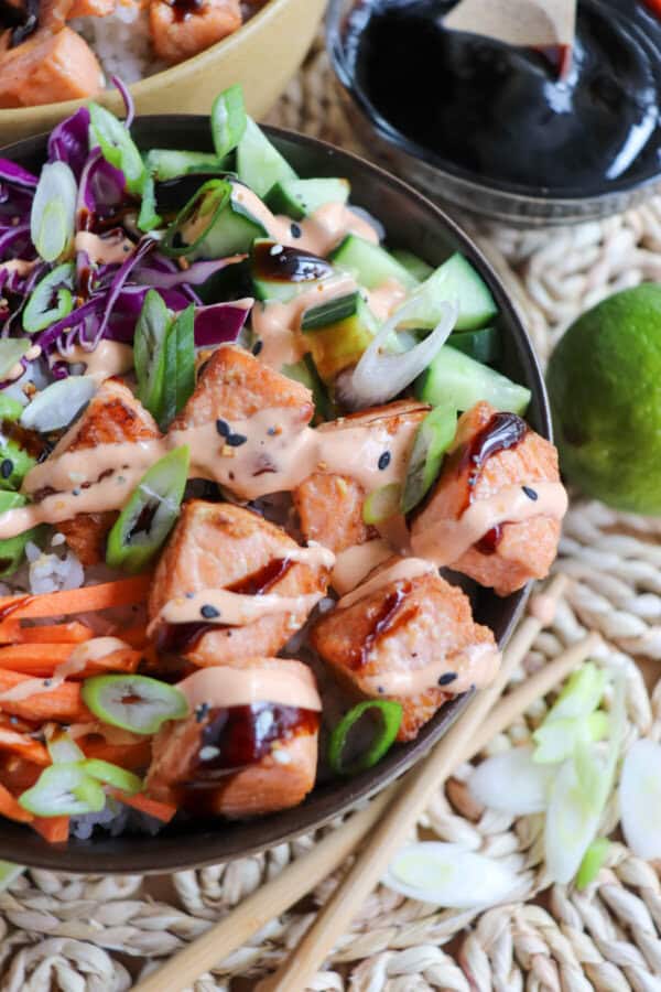 Close up of grilled salmon and vegetables on a bowl of rice drizzled in teriyaki sauce and spicy mayo.