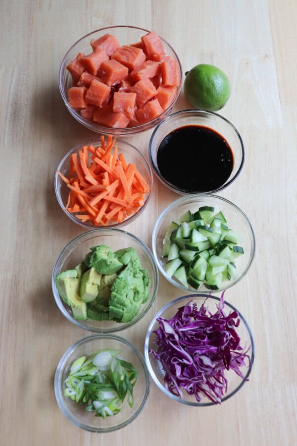 Ingredients for teriyaki salmon bowls in clear glass bowls on a wooden table.