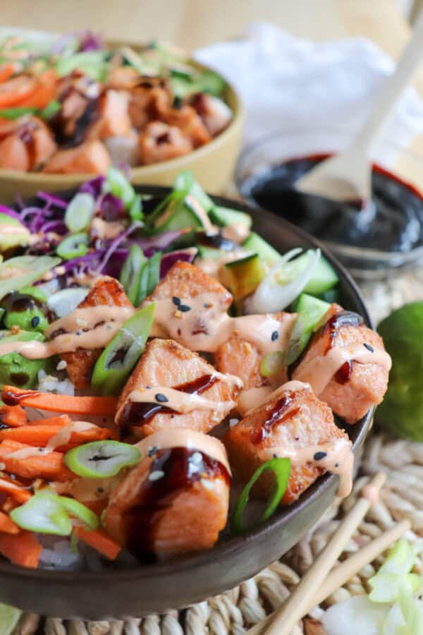 Close up of grilled salmon and vegetables on a bowl of rice drizzled in teriyaki sauce and spicy mayo.