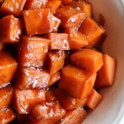 Sweet potatoes covered in a brown sugar glaze in a large white bowl.