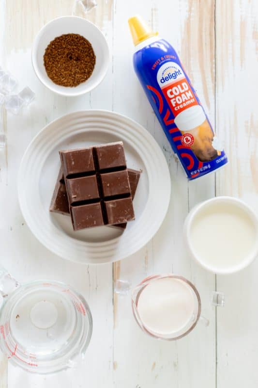 Ingredients for chocolate crackle coffee in clear glass bowls on a white wooden surface.