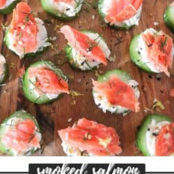 Small rounds of cucumber slices topped with cream cheese, smoked salmon and garnished with fresh dill and lemon zest on a wooden cutting board.