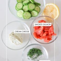 Ingredients for smoked salmon cucumber bites in clear glass bowls on a white counter.