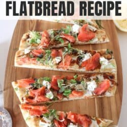A flatbread topped with smoked salmon, mustard greens, goat cheese and balsamic vinegar, cut into strips on a wooden board.