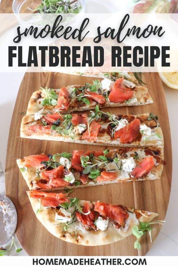 A flatbread topped with smoked salmon, mustard greens, goat cheese and balsamic vinegar, cut into strips on a wooden board.