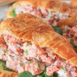 Smoked salmon salad in a fresh croissant with arugula on a wooden cutting board.