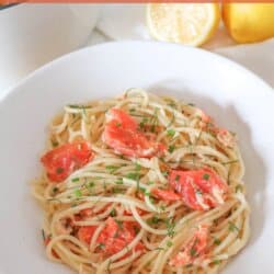 Cooked spaghetti noodles topped with pieces of smoked salmon and garnished with fresh dill in a white bowl.