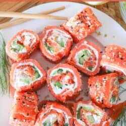 Smoked salmon rolled around cream cheese, cucumbers and avocado and cut into sushi style rolls on a white plate.