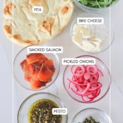 Ingredients for smoked salmon pizza in clear glass bowls on a white surface.