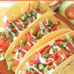 Corn tortillas on an orange plate filled with smoked salmon and diced vegetables drizzled in crema.