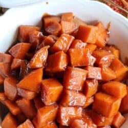 Sweet potatoes covered in a brown sugar glaze in a large white bowl.