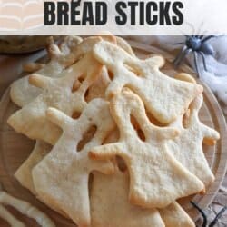 Breadsticks in the shape of ghosts on parchment paper.
