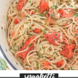 Cooked spaghetti noodles topped with pieces of smoked salmon and garnished with fresh dill in a white dutch oven.