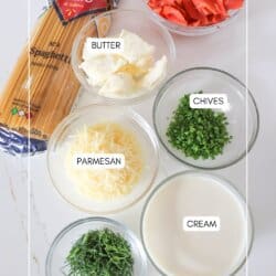 Ingredients for smoked salmon spaghetti in clear glass bowls on a white counter.