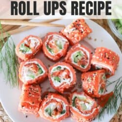 Smoked salmon rolled around cream cheese, cucumbers and avocado and cut into sushi style rolls on a white plate.