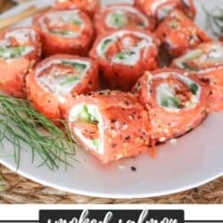 Smoked salmon rolled around cream cheese, cucumbers and avocado and cut into sushi style rolls on a white plate.