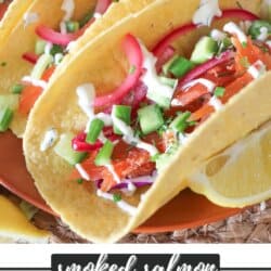 Corn tortillas on an orange plate filled with smoked salmon and diced vegetables drizzled in crema.