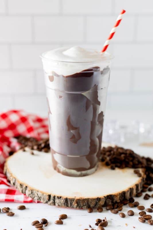 Chocolate coated plastic cup filled with coffee, topped with whipped cream and a red and white striped straw.