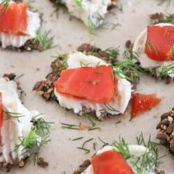 Crackers with cream cheese and pieces of smoked salmon garnished with fresh dill on a cream plate.