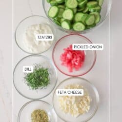 Ingredients for tzatziki cucumber salad in clear glass bowls on a white counter.