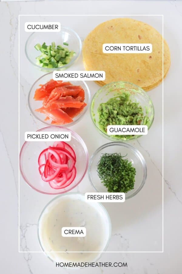 Ingredients for smoked salmon tacos in clear glass bowls on a white counter.