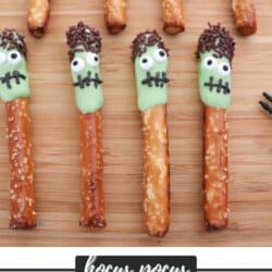 Pretzel sticks half dipped in green chocolate and dipped in brown sprinkles to create hair and placed on a wooden cutting board.