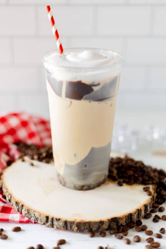 Chocolate coated plastic cup filled with coffee, topped with whipped cream and a red and white striped straw.