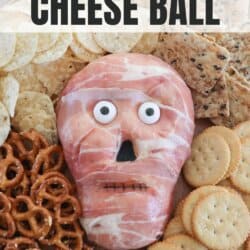 Cream cheese in the shape of a skull wrapped in prosciutto with candy eyes surrounded by pretzels and crackers.