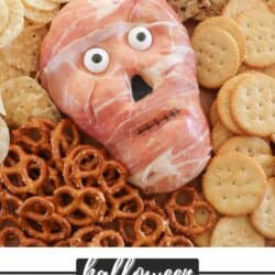 Cream cheese in the shape of a skull wrapped in prosciutto with candy eyes surrounded by pretzels and crackers.