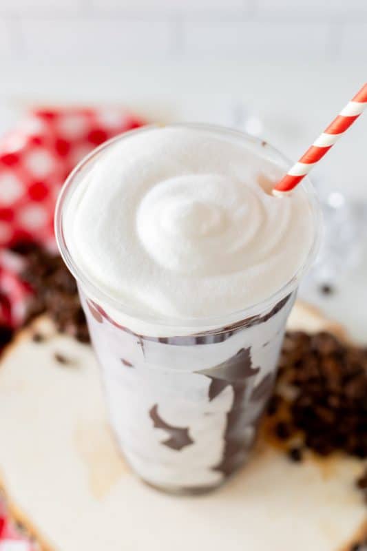 Chocolate coated plastic cup filled with coffee, topped with whipped cream and a red and white striped straw.