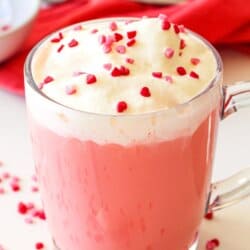 Red velvet hot chocolate in a clear mug topped with whipped cream and sprinkles.