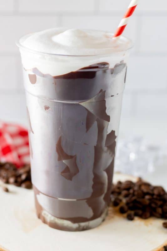 Chocolate coated plastic cup filled with coffee, topped with whipped cream and a red and white striped straw.